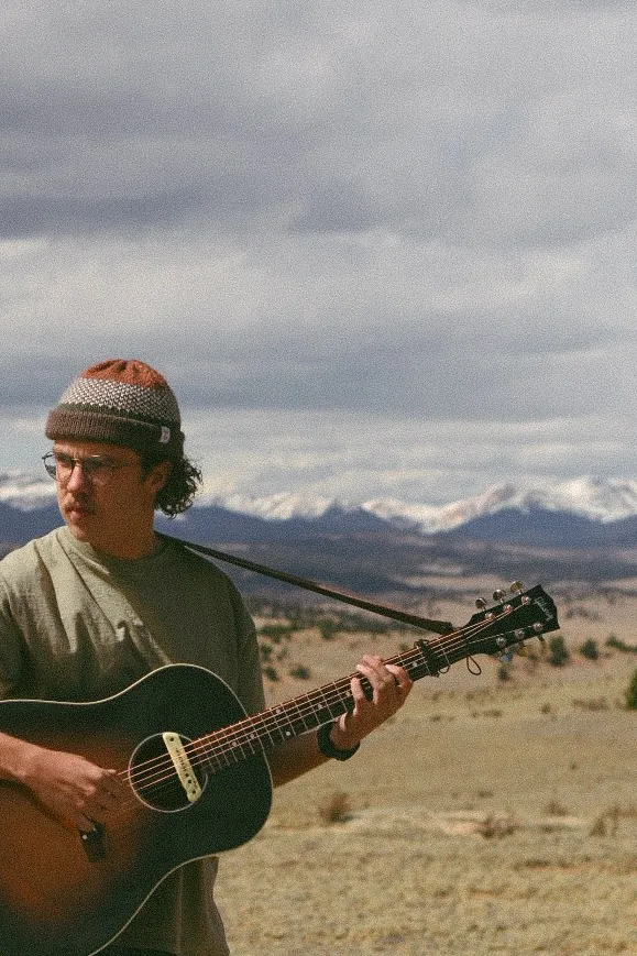 Quincy playing guitar with Colorado mountains behind him